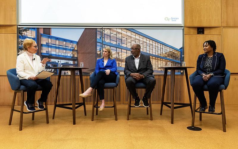 Panel discussion with three speakers and the moderator seated at the front of the room.